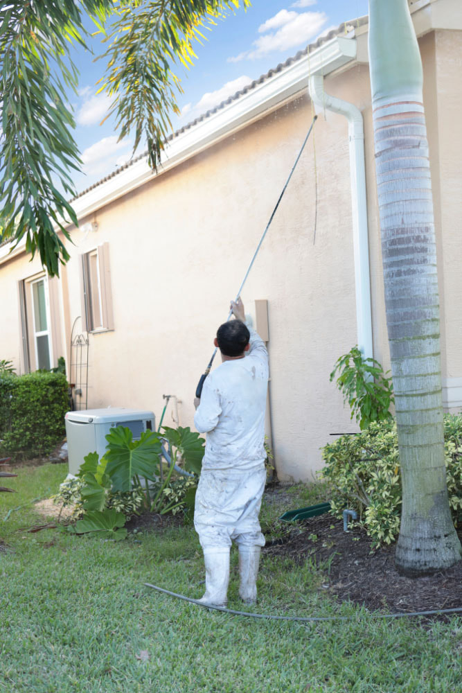 Man cleaning the stucco siding on cream colored house