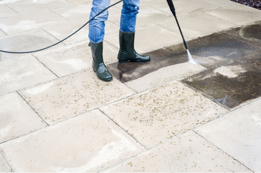 Driveway pavers getting power washed by worker with rubber boots