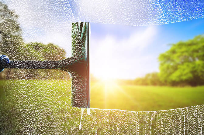 Squeegee across glass pane with grass, trees and blue skies