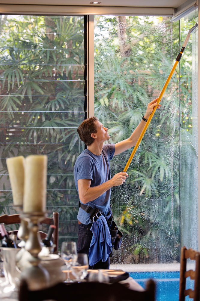 Man holding squeegee on extension pole palm tree in background