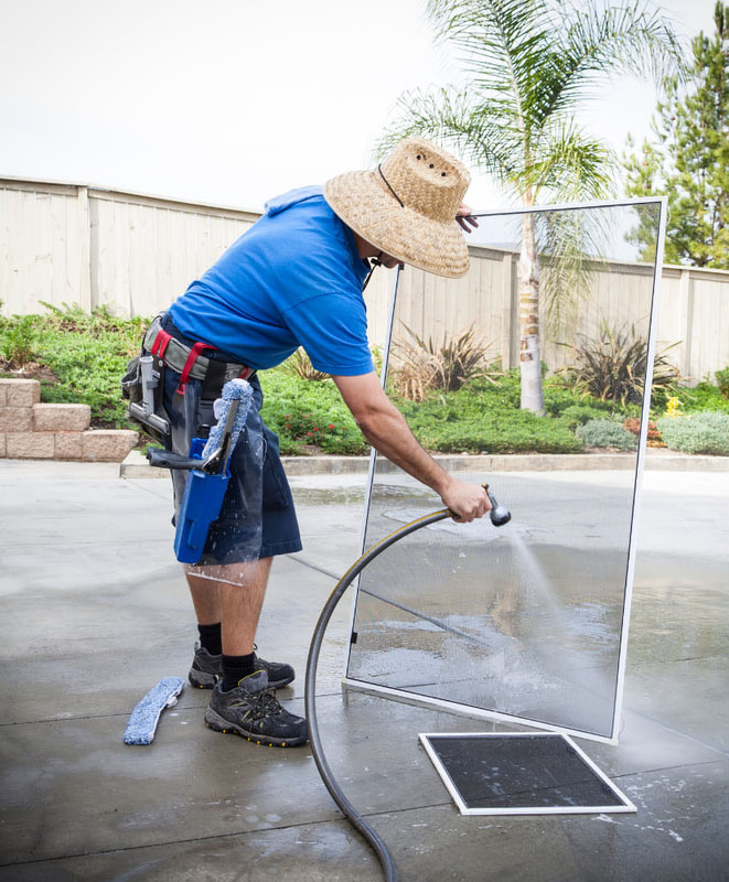 Man washing hosing dirt off of large screen in driveway